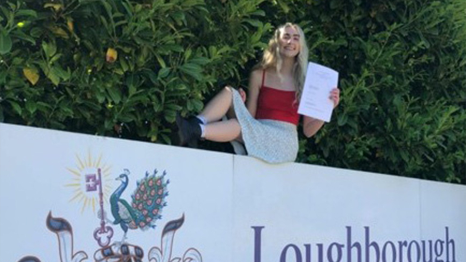 sophie sitting on the loughborough university sign holding her degree certificate